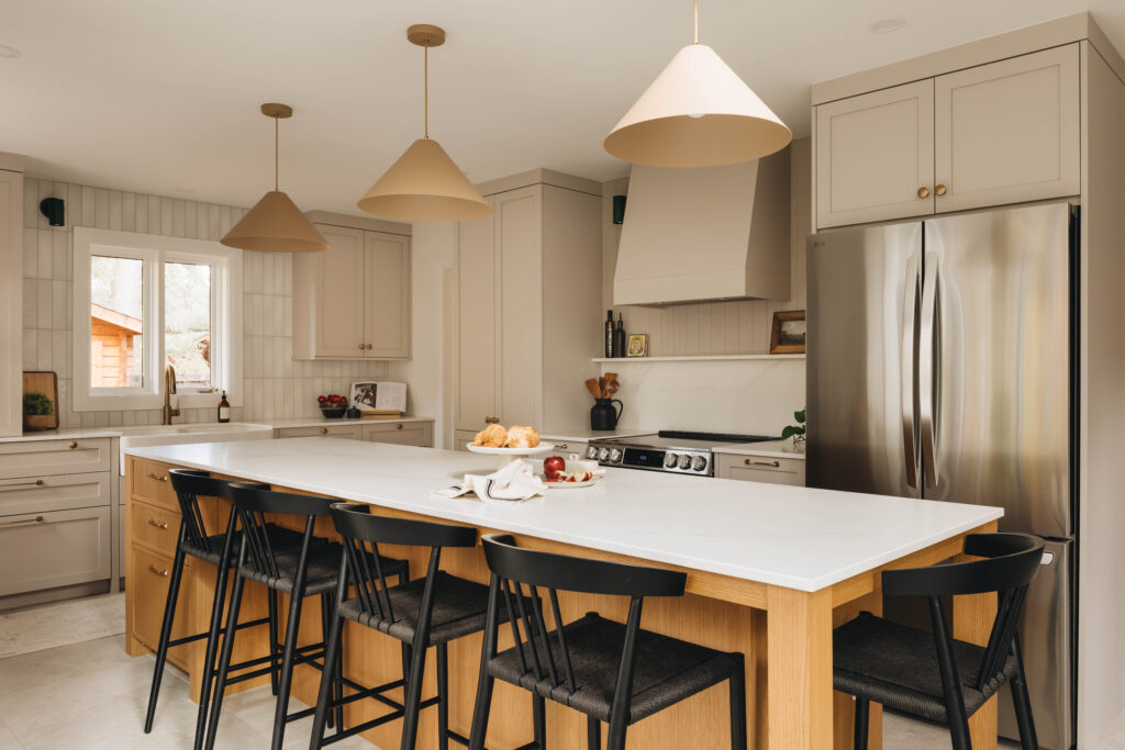 Cuisine élégante sur mesure avec grand îlot en bois, armoires crème, luminaires sculpturaux et ambiance chaleureuse et lumineuse