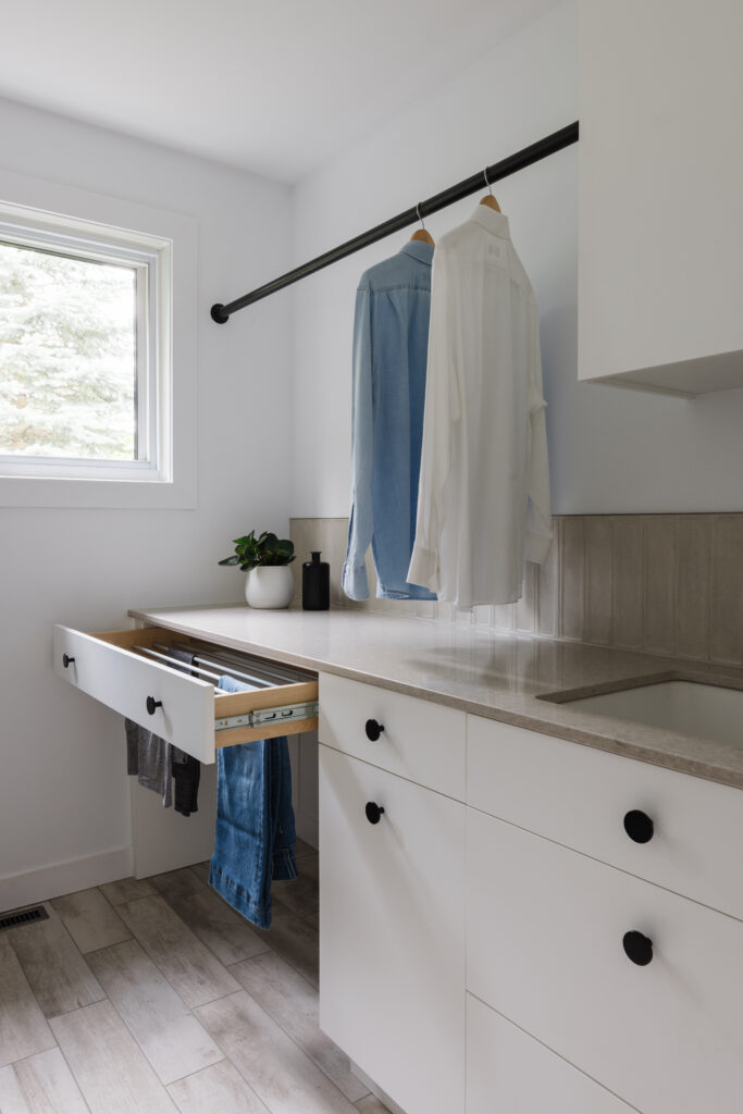 Salle de lavage sur mesure avec armoires blanches, comptoir clair, tringle de suspension, tiroir à linge intégré et espace lumineux
