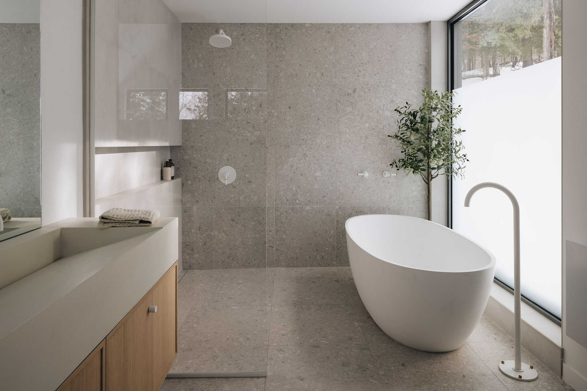 Salle de bain minimaliste sur mesure avec baignoire autoportante, surfaces en béton, meubles en bois clair et grande fenestration
