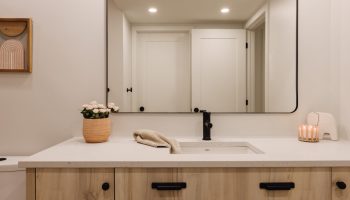 Salle de bain sur mesure au sous-sol avec vanité en bois clair, comptoir blanc, robinetterie noire et design chaleureux et moderne