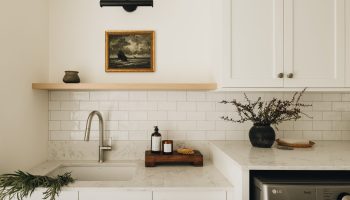 Salle de lavage sur mesure avec armoires blanches, grand plan de travail, évier intégré, électroménagers encastrés et touche de bois chaleureuse