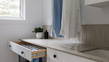 Salle de lavage sur mesure avec armoires blanches, comptoir clair, tringle de suspension, tiroir à linge intégré et espace lumineux