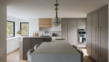 Cuisine moderne sur mesure avec îlot sculptural, armoires pleine hauteur, lignes épurées et lumière naturelle abondante